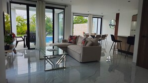 Un salon moderne avec une table basse en verre, un canapé beige et un coin repas comprenant des chaises et une table.