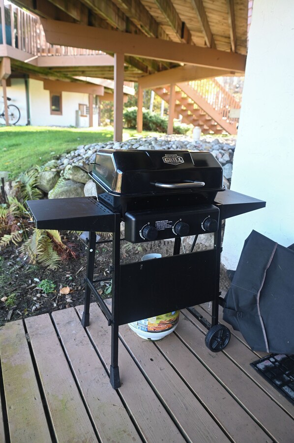 Un barbecue sur une terrasse en bois, avec un mur en pierre et un vélo en arrière-plan.