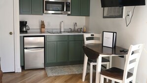 A compact kitchen with green cabinets, a microwave, a refrigerator, a dining table with chairs, and a flat-screen TV mounted on the wall. - New rental! Schuss. Walk to slopes sleeps 4, walk to slopes, Renovated kitchen,  (Mancelona)