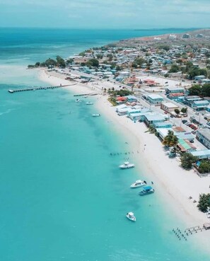 Vue aérienne d’une ville côtière avec une plage, des bateaux et des bâtiments le long de la côte.