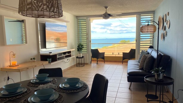 Un soggiorno moderno con angolo pranzo, televisione e vista sulla spiaggia.