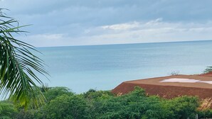 Paesaggio costiero con vista sul mare, una zona erbosa e un sentiero sterrato che conduce a una recinzione in legno.