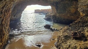 A natural rock arch formation with a beach and ocean view.