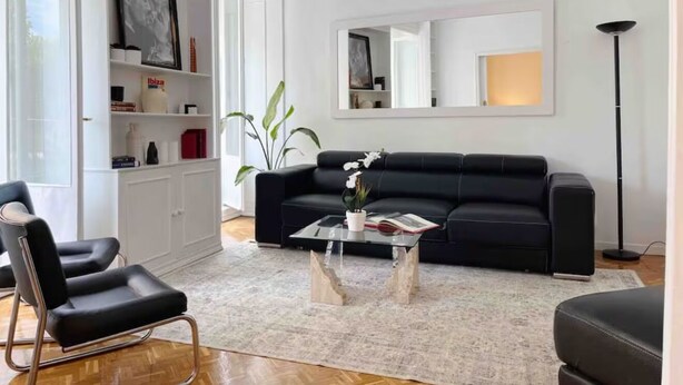 A modern living room with a black leather sofa, a glass coffee table, and a white cabinet with shelves. - Centrally located apartment with Privileged View (Madrid)