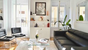A modern living room with a black leather sofa, two black chairs, a glass coffee table, and a white cabinet with decorative items. - Centrally located apartment with Privileged View (Madrid)