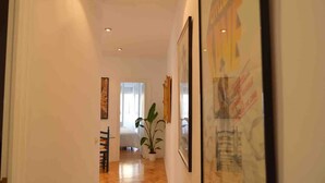A hallway with a wooden floor, a bed with white bedding, a potted plant, and framed artwork on the walls. - Centrally located apartment with Privileged View (Madrid)
