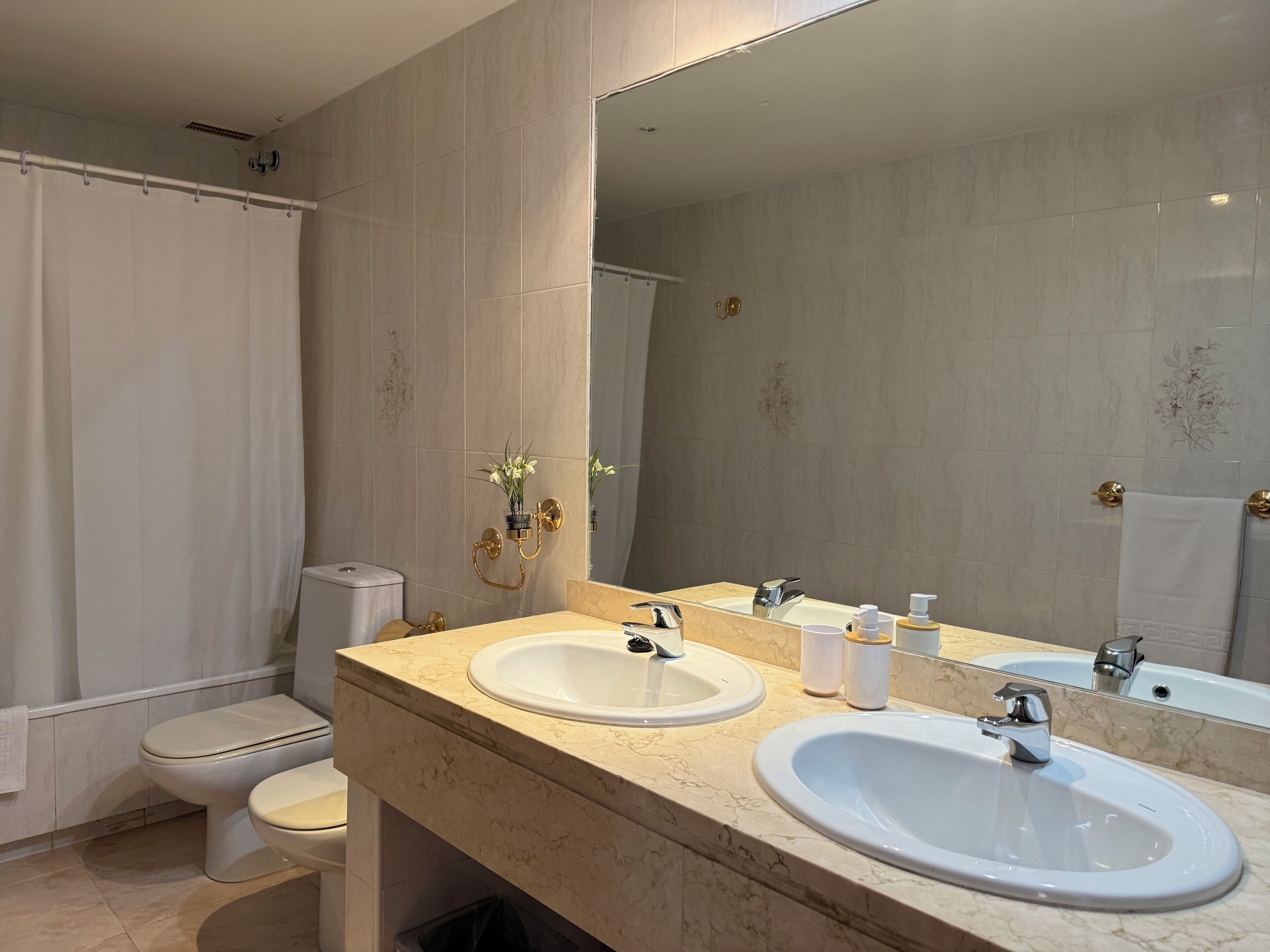 A modern bathroom with two sinks, a toilet, and a shower.