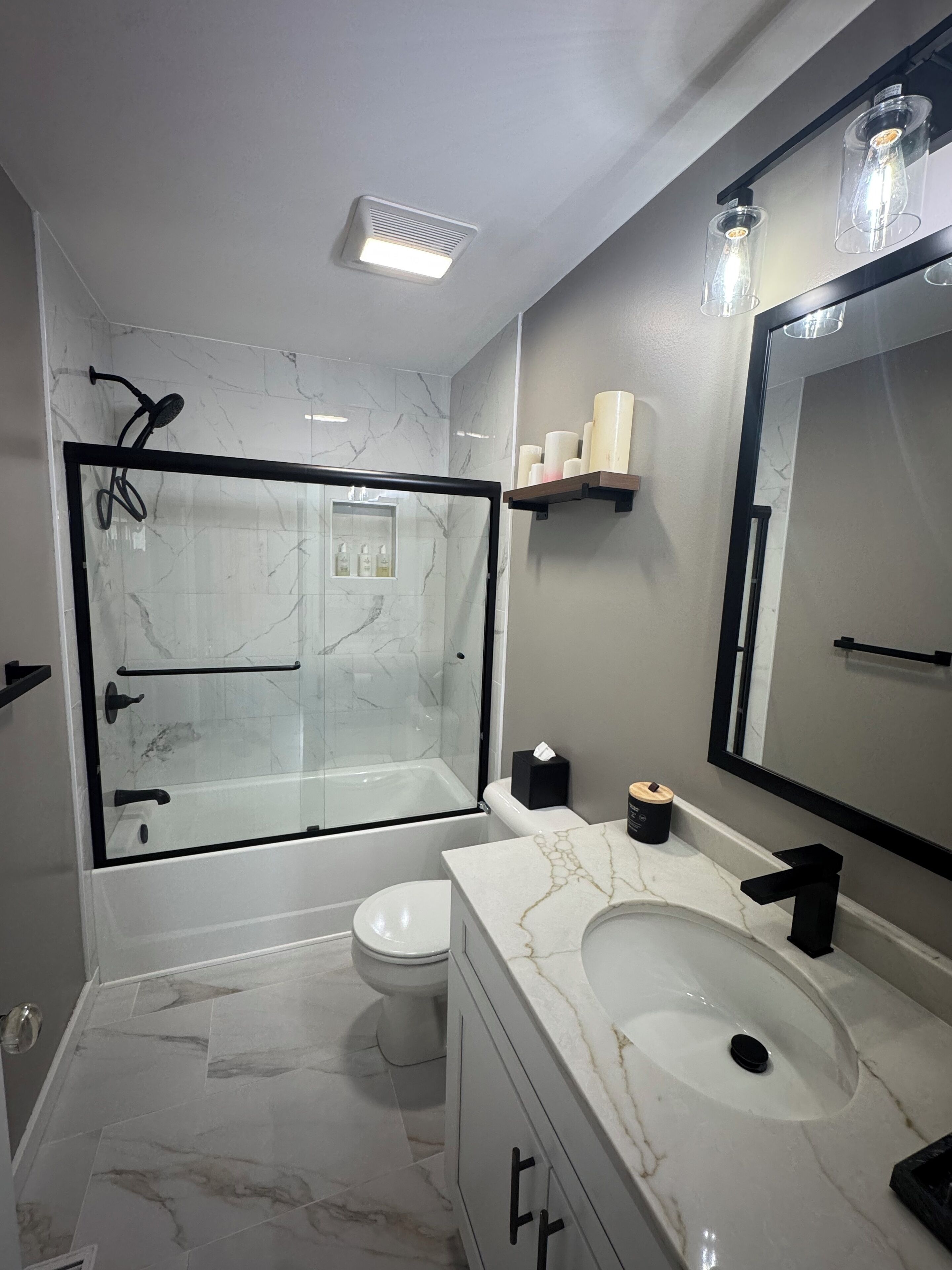 A modern bathroom with a glass-enclosed shower, a white toilet, a marble sink, and a large mirror.