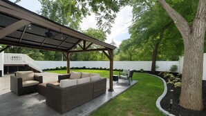 Een overdekt terras met tuinmeubilair, een pergola en een verzorgd gazon.