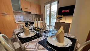A dining area with a table set for two, featuring a patterned tablecloth, two plates, cutlery, glasses, and candles. - Suite Apartment Shuttle • Beach • Garden • WiFi • AirCondition • FreeParking (Nocera Scalo)