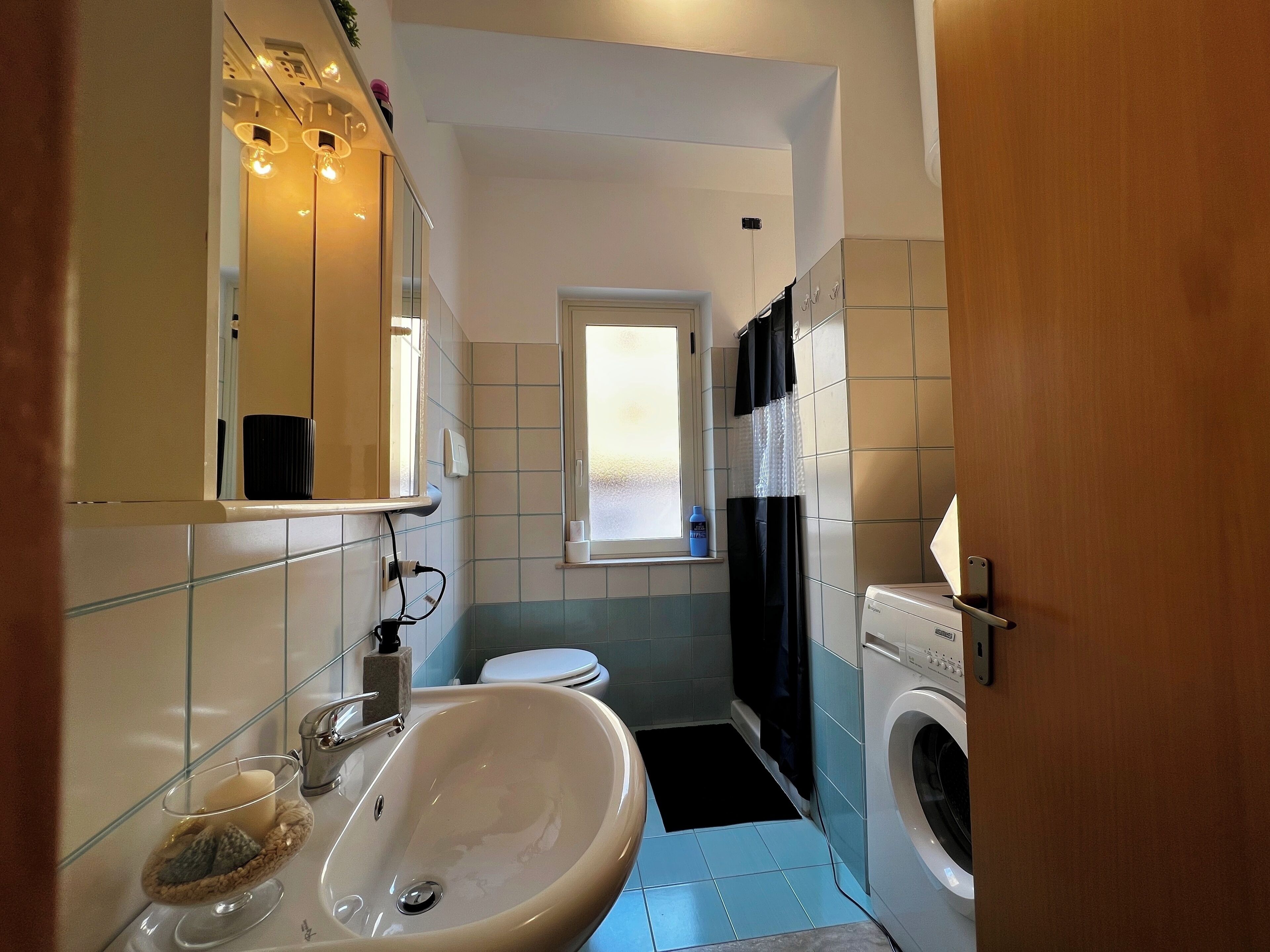 Une petite salle de bain comprenant un lavabo, un miroir, des toilettes et un lave-linge.