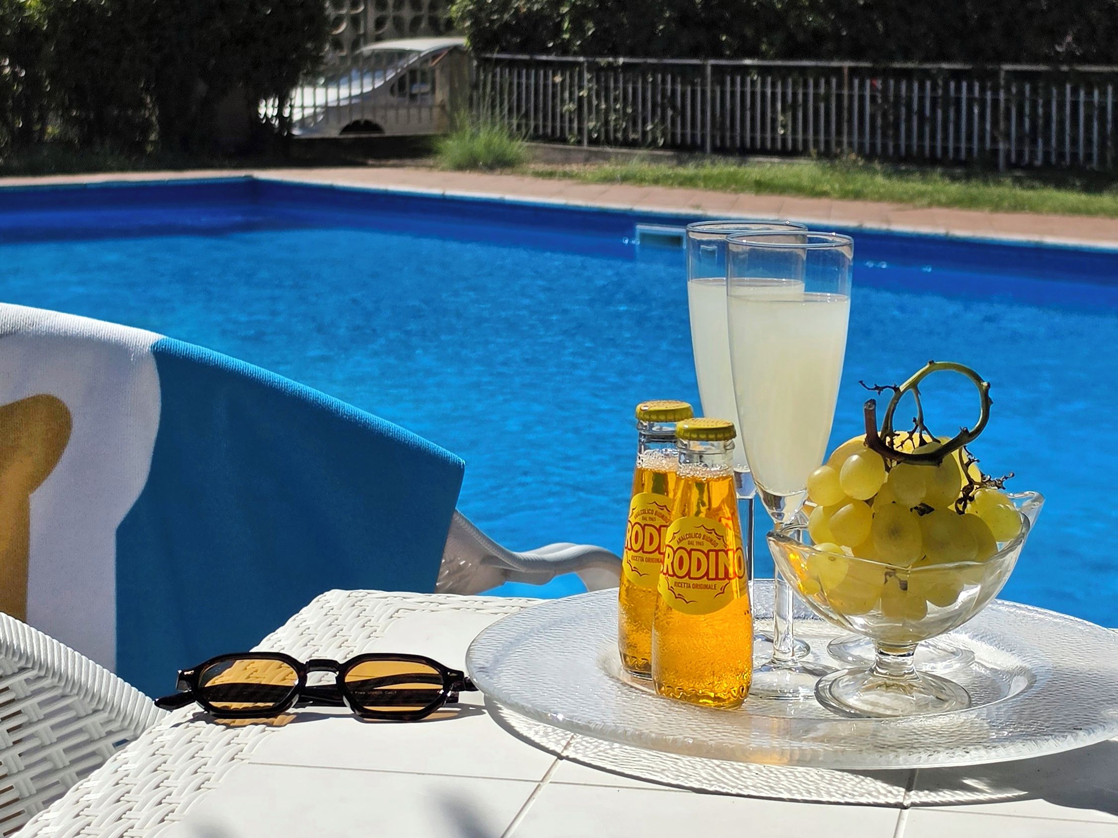 A poolside table with a bottle, a glass, and a bowl of grapes.