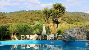 A swimming pool with a view of a mountainous landscape, surrounded by greenery and white plastic chairs. - Suite Apartment Shuttle • Beach • Garden • WiFi • AirCondition • FreeParking (Nocera Scalo)