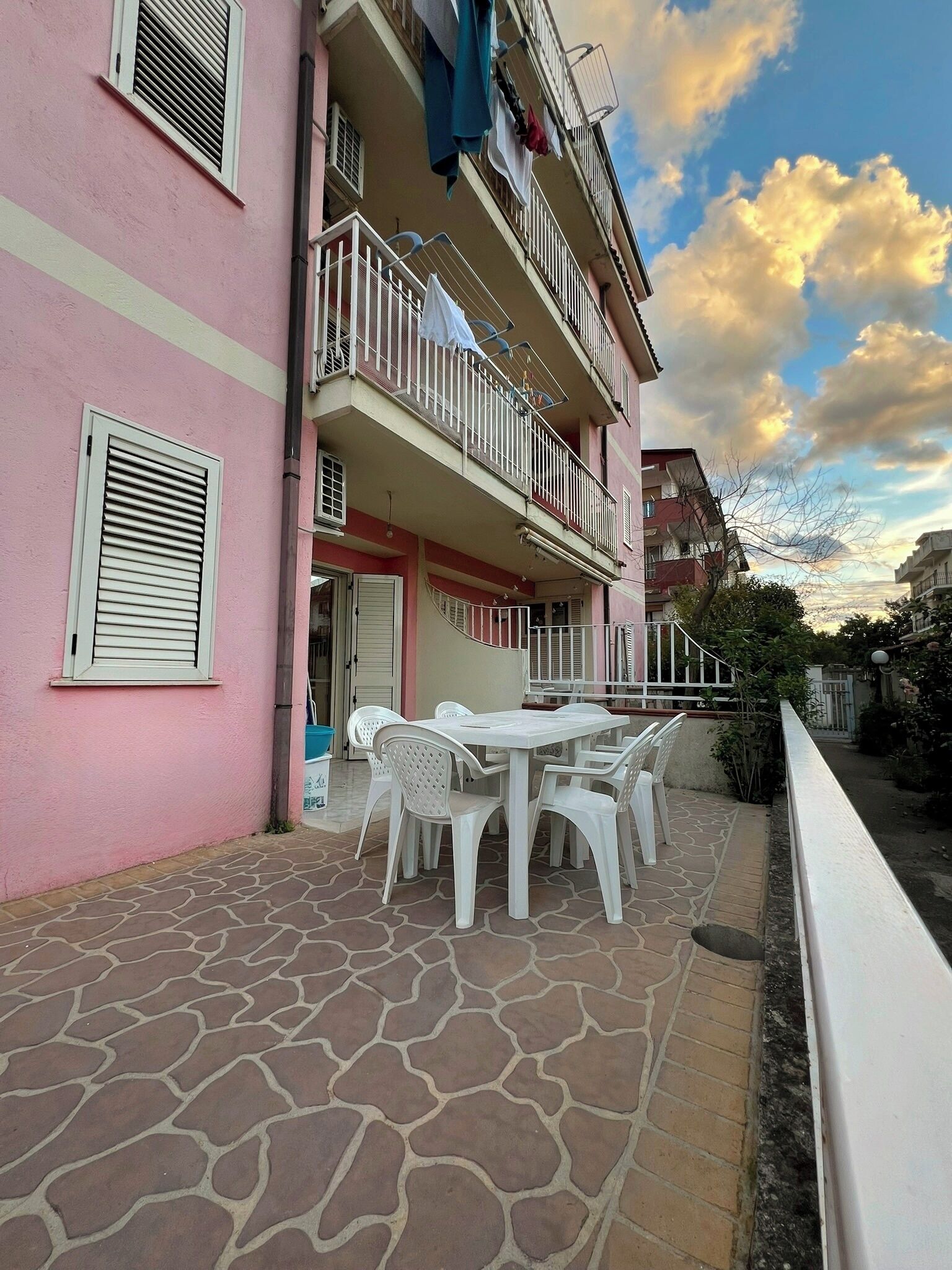 Un bâtiment rose doté d’un balcon, d’un espace extérieur aménagé pour s’asseoir et d’une terrasse carrelée en pierre.