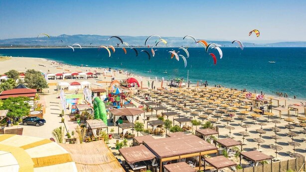 A beach with numerous parasails in the air, a sandy beach area with umbrellas, and a clear blue sky. - Suite Apartment Shuttle • Beach • Garden • WiFi • AirCondition • FreeParking (Nocera Scalo)