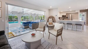 A spacious living area with a large sofa, wicker chairs, a coffee table, and a kitchen with a bar. - Welcoming 3-bedroom house in sunny Naples: Beach Days Made Easy (Naples)