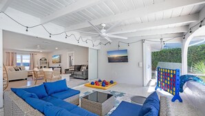 A spacious living area with a large blue sofa set, a coffee table, and a ceiling fan. There is a view of the outdoors through a glass door. - Welcoming 3-bedroom house in sunny Naples: Beach Days Made Easy (Naples)