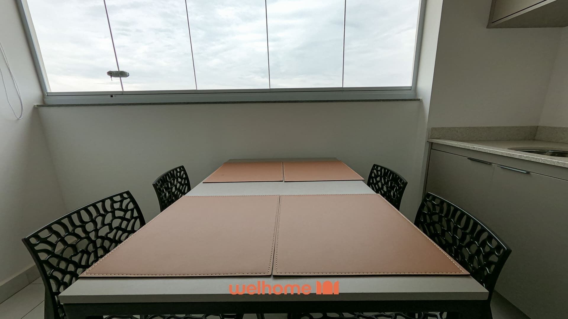 Ein kleiner Essbereich mit Tisch und Stühlen, einem Fenster darüber und einer kleinen Küchenzeile zur Rechten.