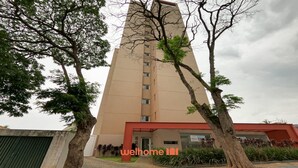 Un edificio alto de color beige con un diseño moderno, rodeado de árboles y un pequeño jardín.