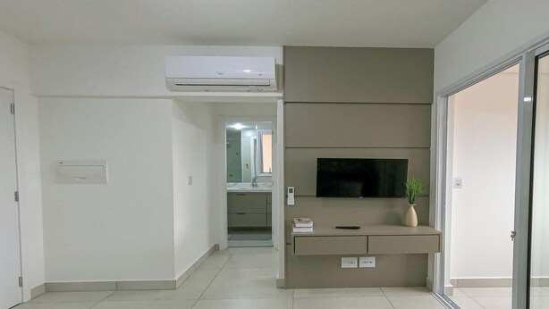 Habitación de hotel moderna con televisor de pantalla plana montado en una consola color beige, una pequeña planta en maceta y una puerta corrediza de vidrio que da a un balcón.
