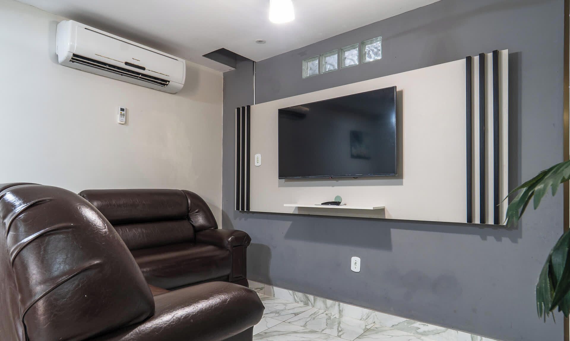 A modern living room with a leather sofa, a mounted flat-screen TV, and an air conditioning unit.