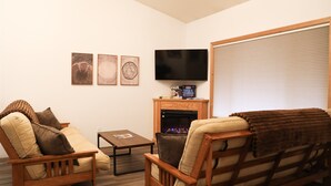 A living room with two wooden chairs, a small table, a fireplace, and a television mounted on the wall. - Serene Morning Meadow Condo  #93, at Wallowa Lake (Joseph)