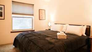 A hotel room with a bed, a window with blinds, a nightstand with a lamp, and a framed picture on the wall. - Serene Morning Meadow Condo  #93, at Wallowa Lake (Joseph)