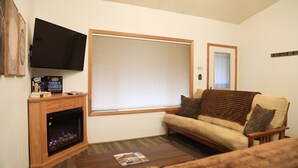 A living room with a fireplace, a sofa, a coffee table, and a television mounted on the wall. - Serene Morning Meadow Condo  #93, at Wallowa Lake (Joseph)