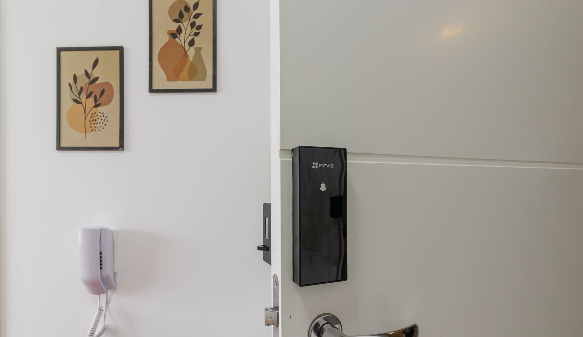 A hotel room with a white wall, a black EZVIZ intercom, and a white telephone.