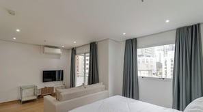 Ein modernes Hotelzimmer mit einem großen Bett, einem an der Wand montierten Fernseher, einer Couch und einem Fenster mit Vorhängen.