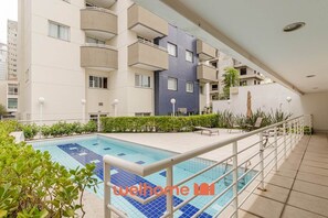 A swimming pool with a tiled deck, surrounded by a white railing and greenery. - Apartamento na Bela Vista perto do Sirio Libanes (São Paulo)