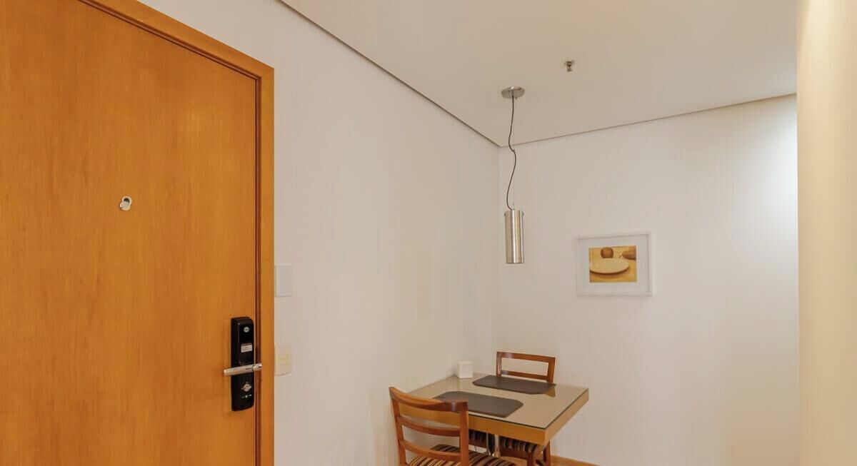 Een kamer met een houten deur, een tafel met stoelen, een hanglamp en een lijst met een foto aan de muur.