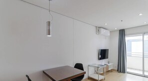 Una habitación de hotel moderna con una mesa de madera, una silla negra, un mueble de televisión de vidrio y un ventanal con vistas a la ciudad.