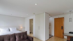 Moderni hotellihuone, jossa on sänky, sohva, vaatekaappi ja työpöytä.