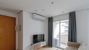 Een moderne woonkamer met een flatscreen televisie op een houten standaard, een bank en een schuifdeur naar een balkon.