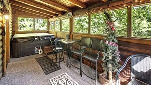 A cozy cabin interior with a hot tub, seating area, and large windows overlooking a forest. - Affordable Pigeon Forge Cabin 1 Mile to Strip! (Pigeon Forge)