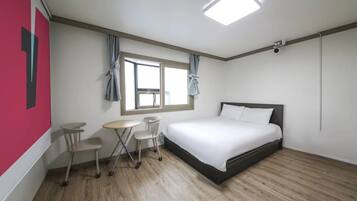 A hotel room with a bed, a small table, two chairs, a window with curtains, and a ceiling light.