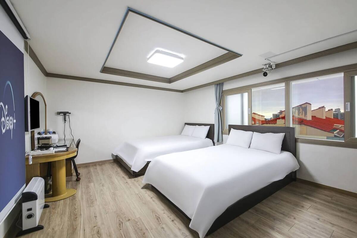 Une chambre d’hôtel avec deux lits, un bureau avec un ordinateur, un téléviseur à écran plat et une grande fenêtre donnant sur la ville.