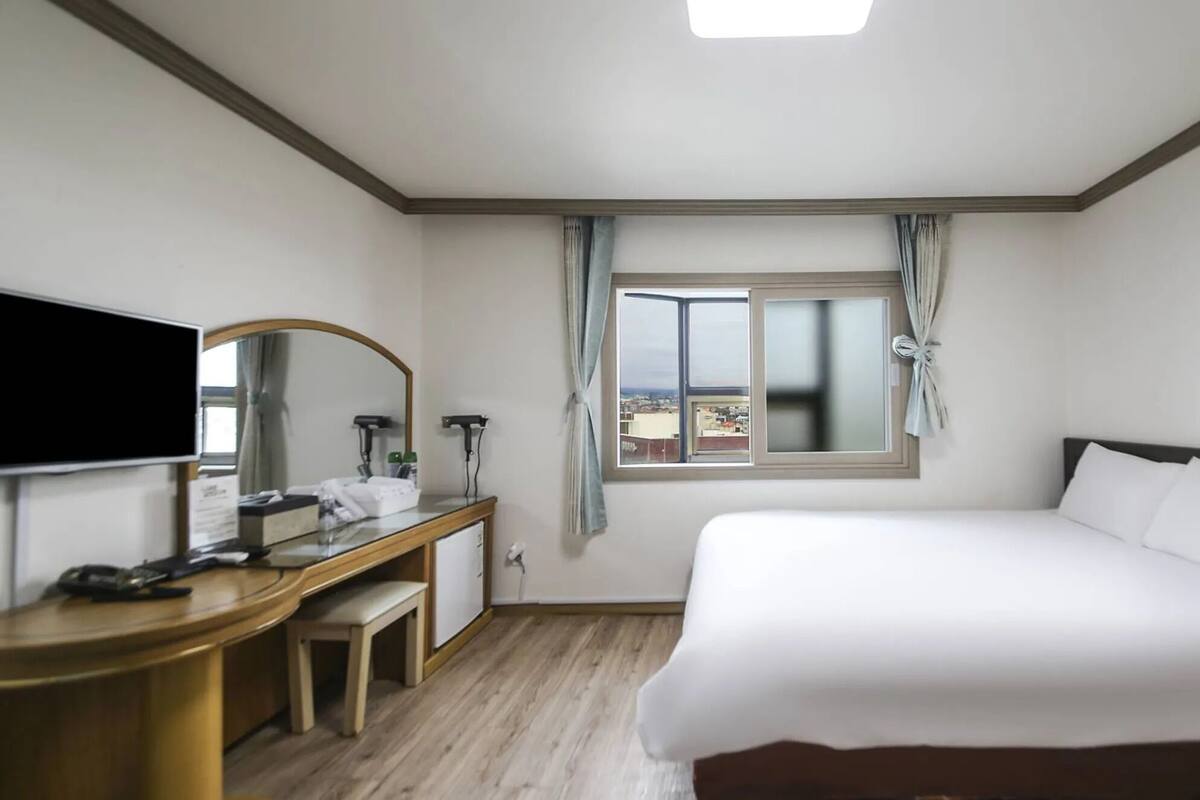 Une chambre d’hôtel avec un lit, un bureau et une chaise, une télévision et une fenêtre avec des rideaux.