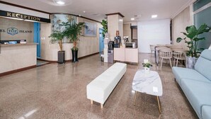A hotel reception area with a reception desk, a seating area with a sofa and a coffee table, and a dining area with a table and chairs. - Top Island Hotel (Jeju City)