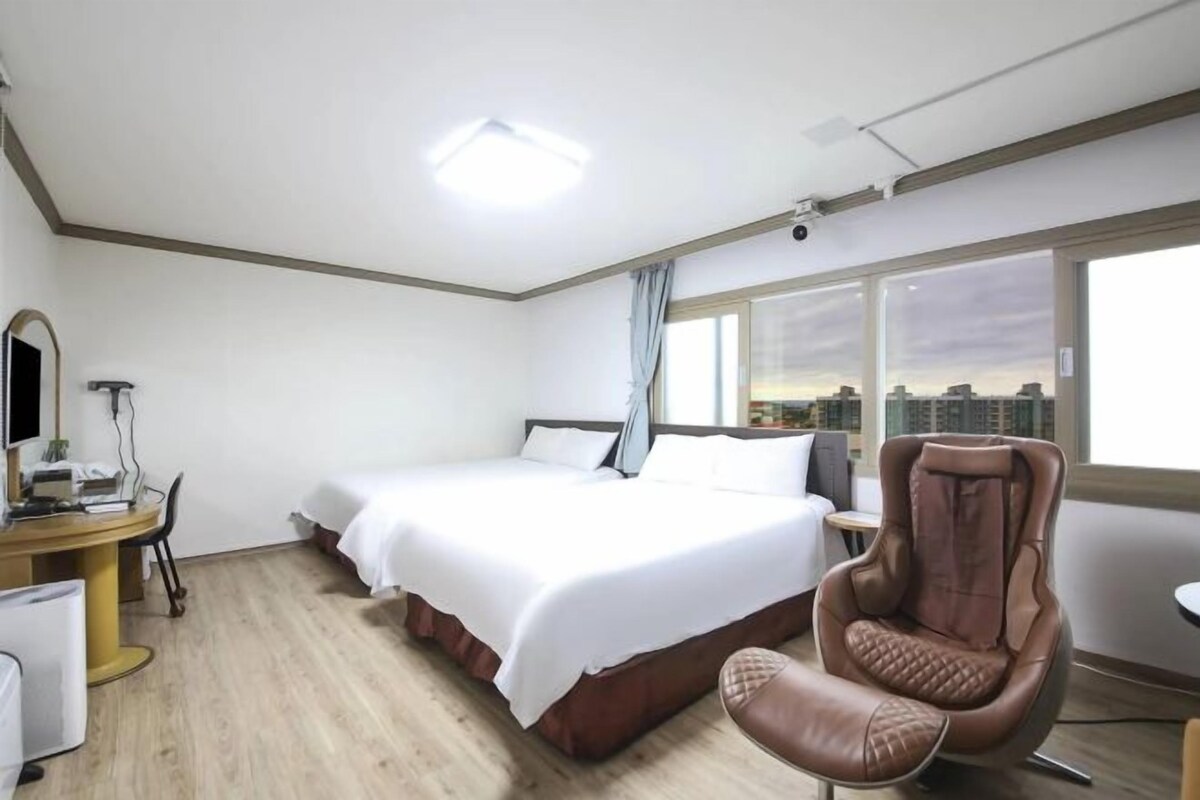 Une chambre d’hôtel avec un lit, un bureau équipé d’un ordinateur, une chaise et une grande fenêtre donnant sur la ville.