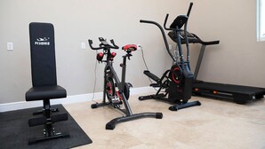 Un gimnasio en casa con bicicleta estática, elíptica, cinta de correr y una banca.