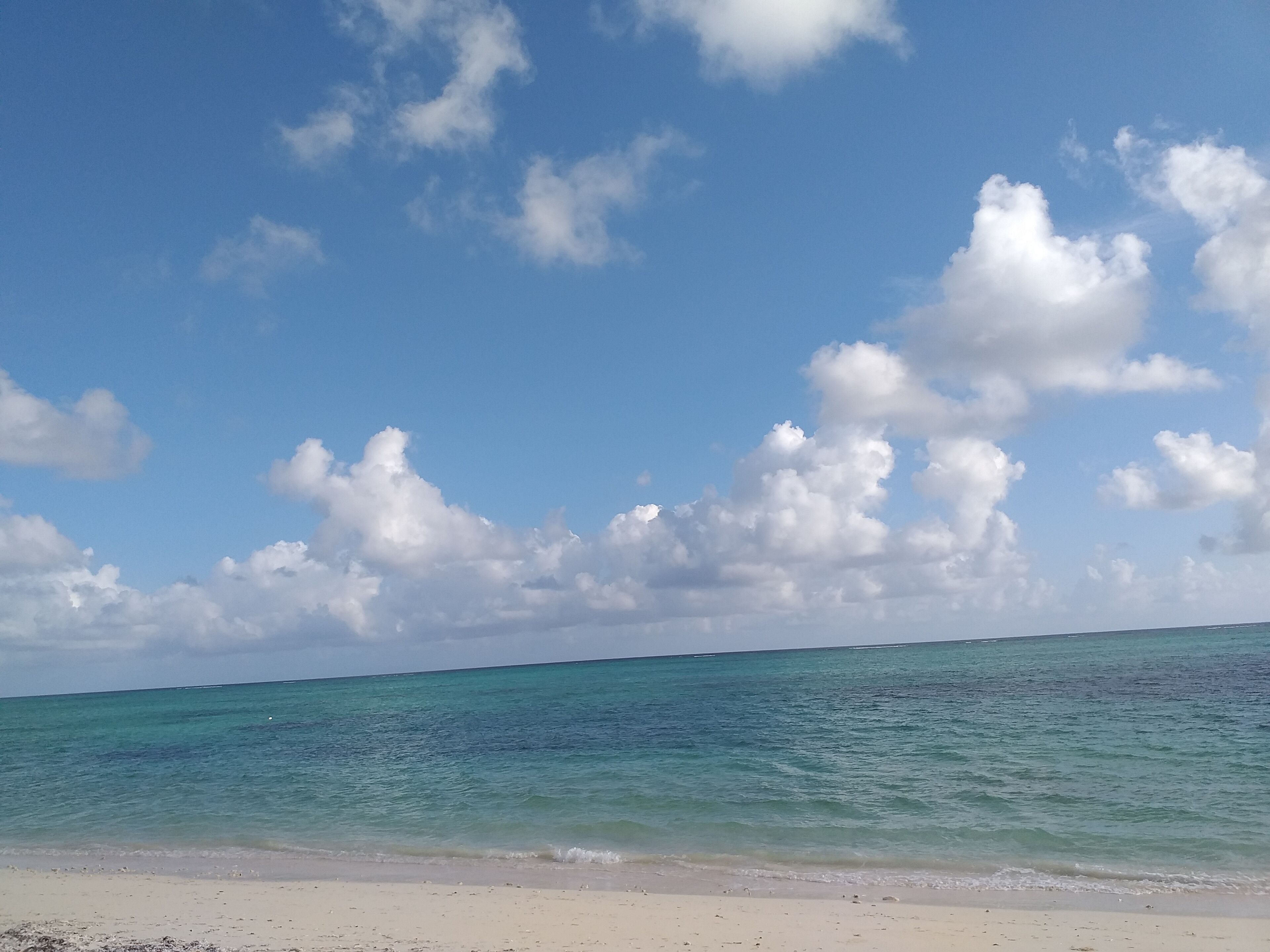 A beach with clear turquoise water and a sandy shore under a partly cloudy sky.
