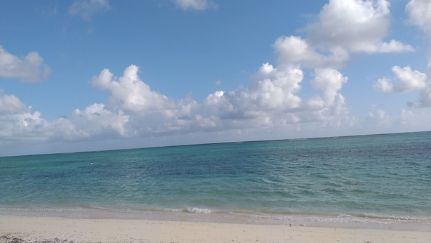 Una spiaggia con acqua cristallina dai riflessi turchini e una riva sabbiosa, sotto un cielo parzialmente nuvoloso.