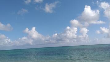 A beach with clear turquoise water and a sandy shore under a partly cloudy sky.