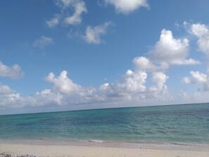 Una playa con agua turquesa cristalina y una orilla arenosa bajo un cielo parcialmente nublado.