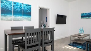 Un comedor con una mesa y sillas, un televisor de pantalla plana montado en la pared y una mesita con un objeto decorativo.