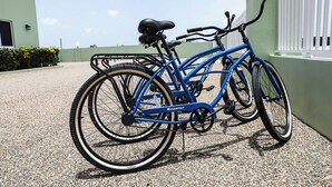 Una bicicletta blu parcheggiata su fondo di ghiaia vicino a un edificio con una recinzione bianca.