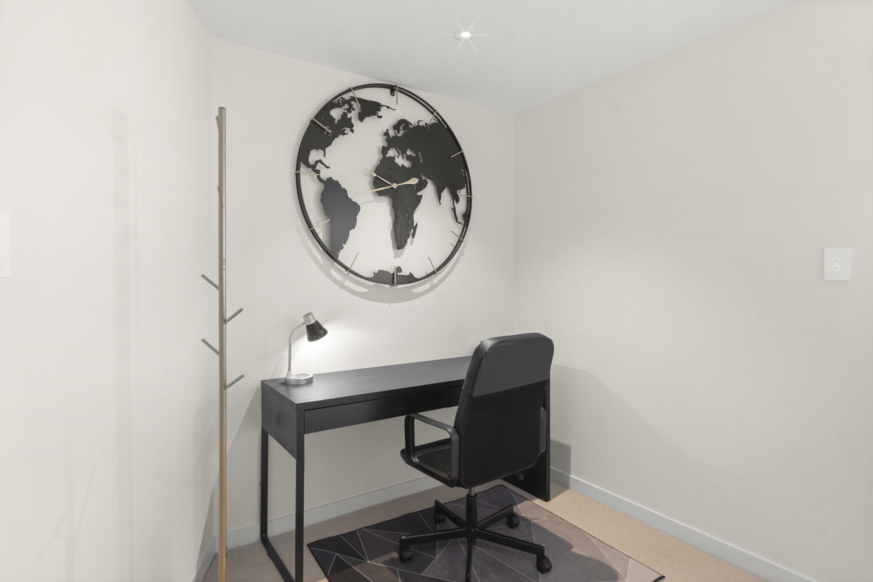 A modern office space with a black desk, a black office chair, and a world map clock on the wall.
