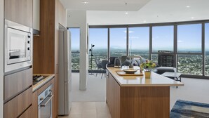 Une cuisine moderne dotée d’un grand îlot central, d’un coin repas avec des chaises et offrant une vue sur le paysage urbain grâce à de grandes fenêtres.